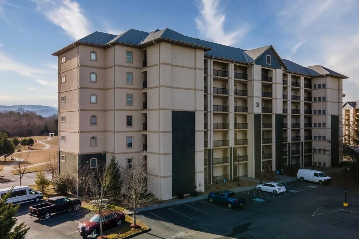 A welcoming exterior shot of the multi-story condo building, with a well-maintained parking area and the surrounding landscape visible. The image captures a sense of arrival and highlights the easy access and community aspect of the property.