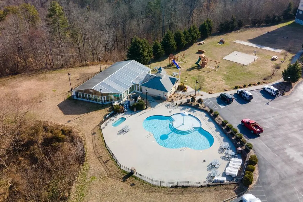 An expansive recreational area with a vibrant outdoor swimming pool, children playing on a playground, and the condo building in the background. The scene includes families gathering for barbecues, kids splashing in the pool, and people enjoying the play structures, capturing an atmosphere of lively, multi-generational fun.