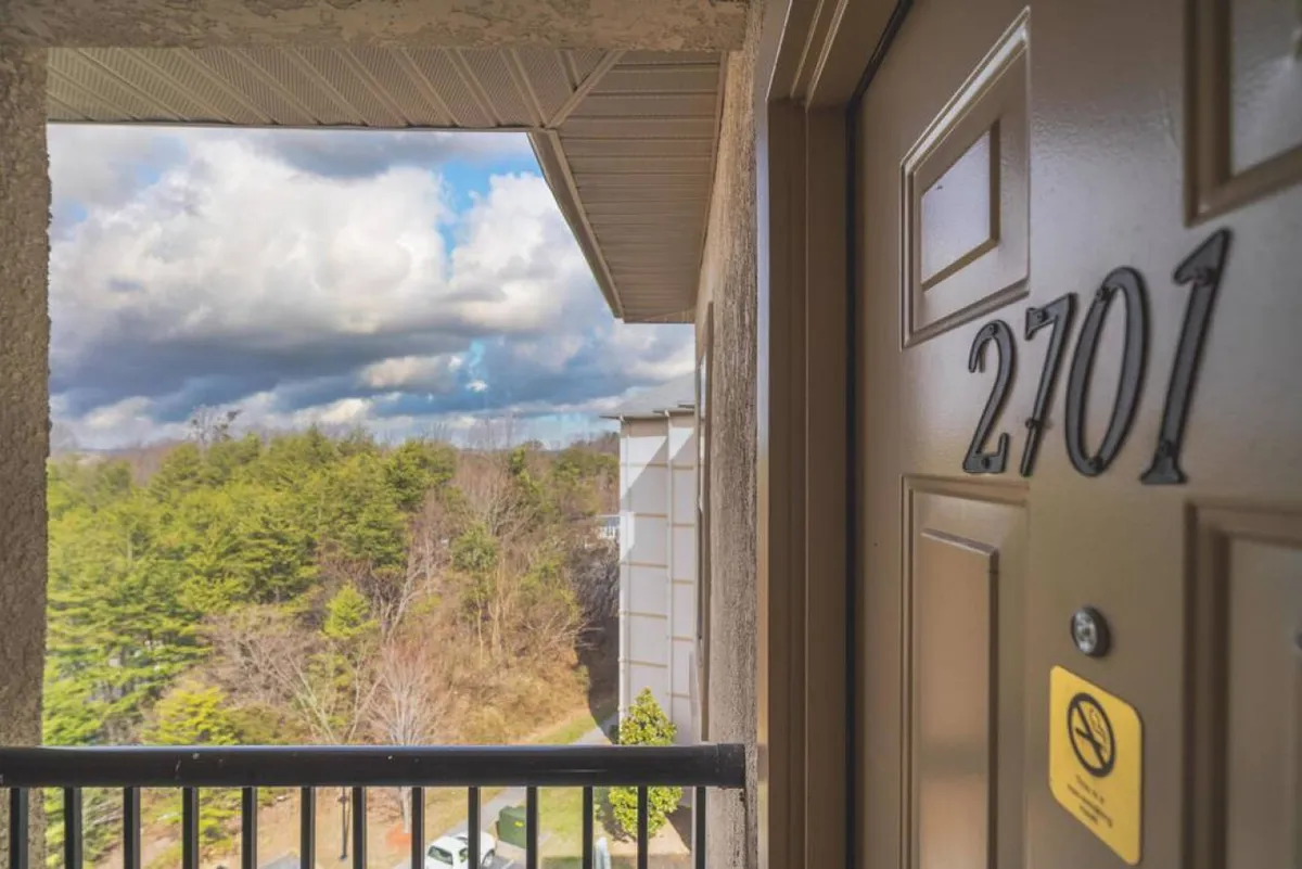 A view of an exterior door numbered 2701, with a balcony railing and a backdrop of trees and open sky. The scene feels residential yet connected to nature, subtly suggesting quick access to the outdoors and nearby excitement.