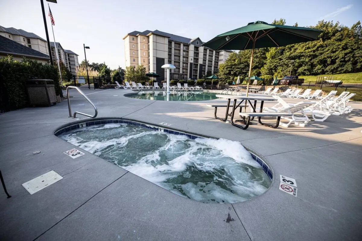 This exterior image centers on a lively pool area featuring a swimming pool, hot tub, lounge chairs, a picnic table, and umbrella. The setup is ideal for families, offering both leisure and play opportunities in a sunny, outdoor environment.