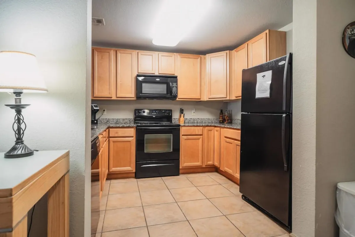 A cozy kitchen with granite countertops, black appliances, wooden cabinets, and a lampshade providing soft lighting. The kitchen is inviting, well-equipped, and ready for meal preparation or casual coffee chats.