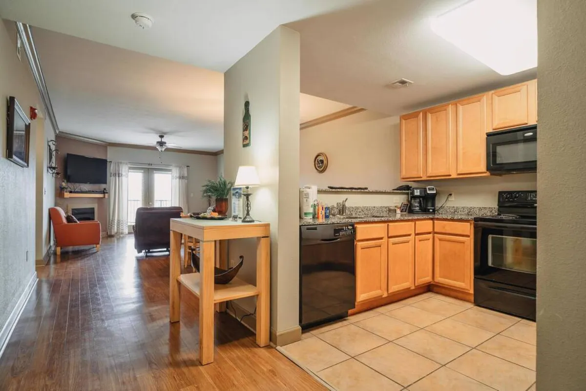 This image features a bright, open-concept interior where the kitchen, dining area, and living room are seamlessly connected. Kitchen cabinetry and countertop appliances are visible, alongside the dining area and a view of the living room, emphasizing the social and communal atmosphere of the space.