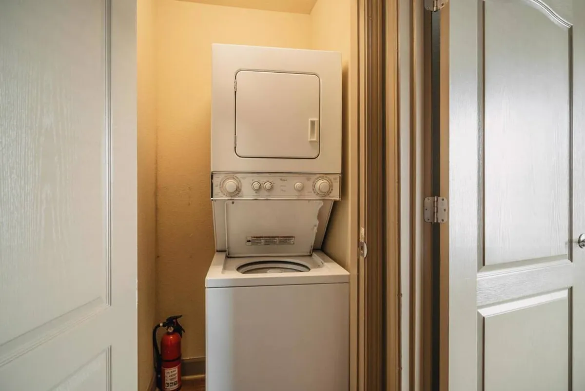 This practical interior scene spotlights a stacked washer and dryer, along with a fire extinguisher and doorways to adjacent spaces. It conveys the convenience and thoughtful touches that make family stays seamless and stress-free.
