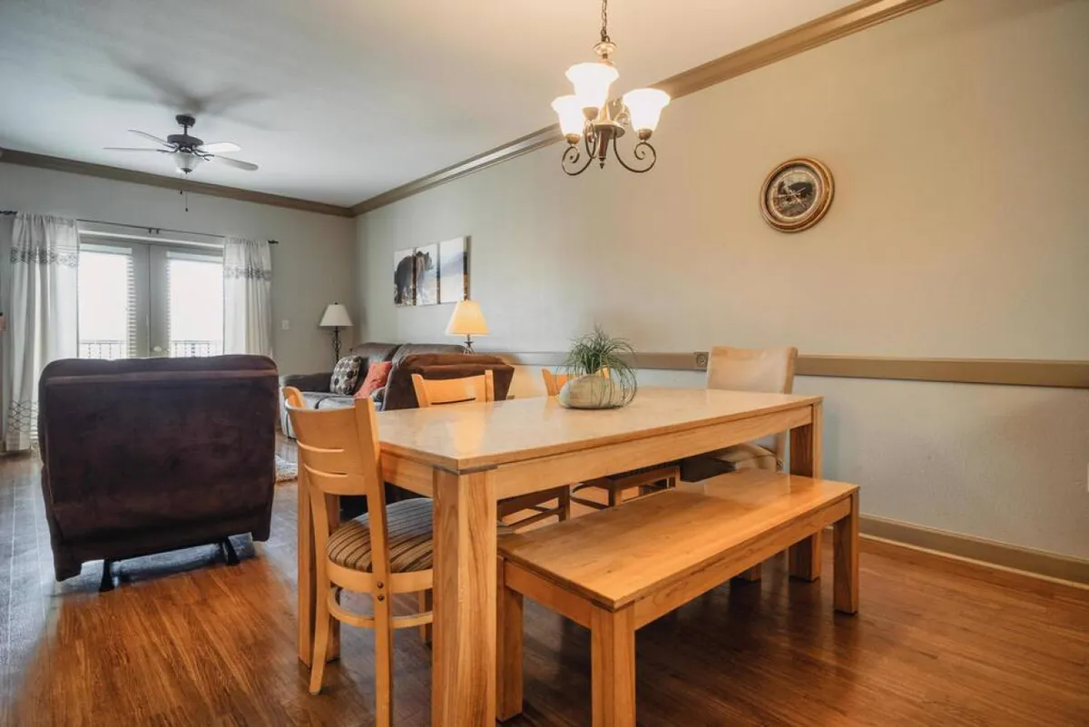 A warmly lit dining and living space with a dining table, chandelier, comfortable sofa, and window curtains. The setup suggests a welcoming area for family meals, holiday celebrations, and casual get-togethers.